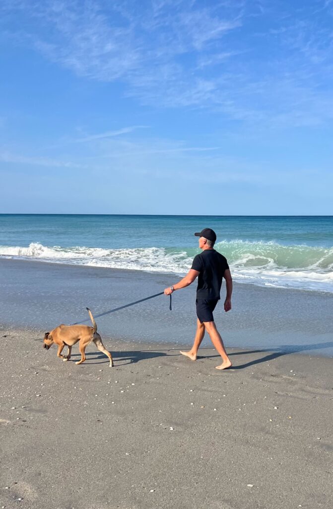 Dave walking his dog, Sasha, on the beach while wearing a leash